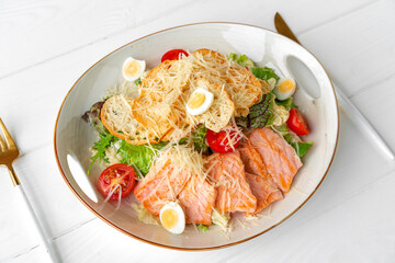 Caesar salad with grilled chicken on white wooden background