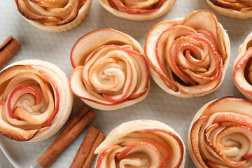 Obraz na płótnie Canvas Freshly baked apple roses and cinnamon sticks on plate, flat lay. Beautiful dessert