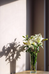 White lilies in a transparent vase on the background of the wall.