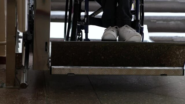 A disabled young man in a wheelchair ascends on an automatic electric ramp. Close up of wheelchair wheel and disabled person's legs.
