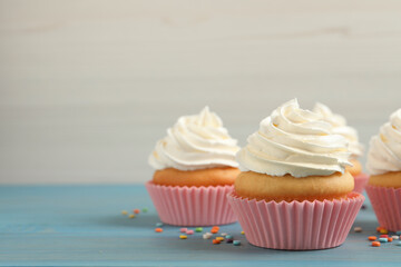 Delicious cupcakes decorated with cream on light blue wooden table, space for text