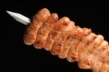 Barbecue chicken sausages on skewers on black background.