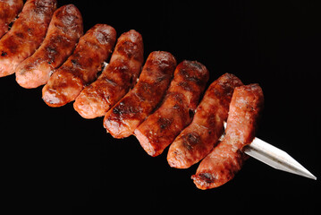 Barbecue sausages on skewers on black background. - obrazy, fototapety, plakaty