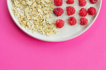 Ripe raspberry fruits with oatmeal flakes on plate, healthy pile of summer berries top view. Healthy proper breakfast concept with free copy space for text