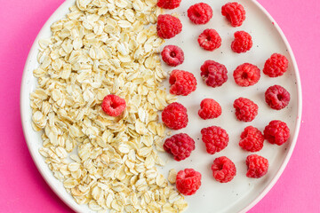 Ripe raspberry fruits with oatmeal flakes on plate, healthy pile of summer berries top view. Healthy proper breakfast concept with free copy space for text