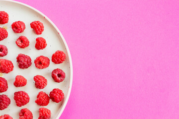 Ripe raspberry fruits on plate, healthy pile of summer berries  top view. Pattern flat lay of red scarlet  raspberry on pink background with free copy space for text