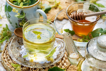 Linden flowers tea in a glass cup and teapot on a white napkin, on a white tablecloth background, yellow drink of linden flower with linden blossoms honey, healthcare and healthy eating concept