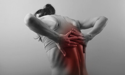 Young strong sporty woman suffering  and holding the hands her back, pain in the back, pain in the spine, highlighted in red.. The concept of medicine, massage, physiotherapy. Rear - 445001398