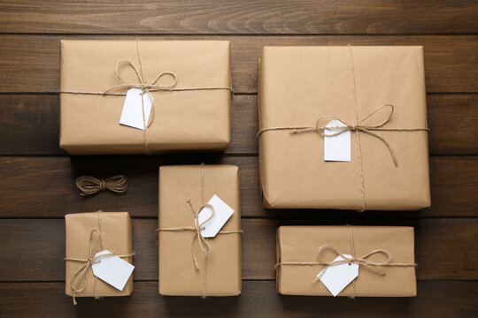 Parcels wrapped in kraft paper with tags on wooden table, flat lay
