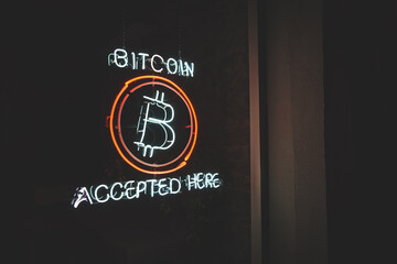 Bitcoin accepted here cryptocurrency led neon sign in a window of small business at night with copy...