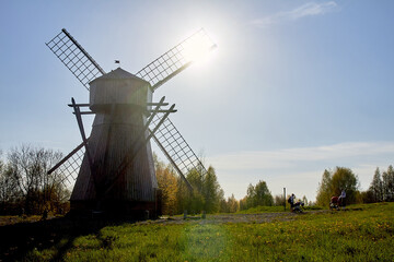 An old wooden windmill stands in a field near the forest