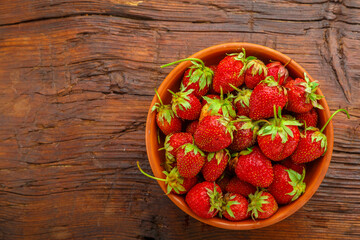 Ripe strawberries in a clay plate on a wooden table.