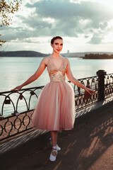 a young elegant female ballerina in a pink dress with a full organza skirt, a ballerina poses near...