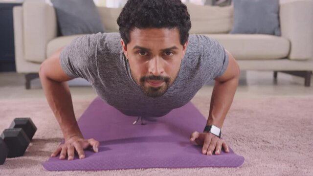 Camera follows man in fitness clothing up and down as her does press ups on mat in lounge at home - shot in slow motion