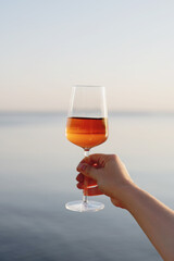 Female hand holding a glass of wine on background of sunset at the sea.