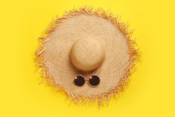 Straw hat and sunglasses on yellow background, flat lay. Stylish headdress