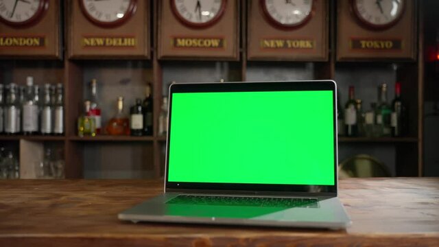 Laptop with green scree on a table in a vintage bar. Easy replace the green screen with your graphics, photos, videos or website.