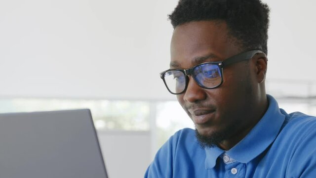 Young positive afro businessman working at desk in office with laptop.