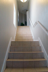 Looking up a tall narrow tiled stairwell with white walls and  handrail.