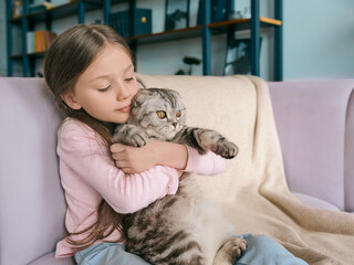 Fototapeta na wymiar Adorable, cute, smiling girl hugging Scottish gray cat on the sofa at home. Pets, friendship, home, happiness concept 