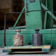 A closeup of a vintage, green weighting machine and two iron weights. 