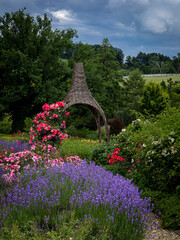 A wicker gazebo in the garden, surrounded with blooming flowers. 