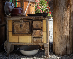 A vintage, rust-eaten kitchen stove with an old kettle, frying pan and other kitchen utensils, standing outdoors. 