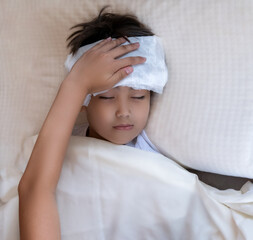 Child boy lies in bed with closed eyes with white cool fever on his forehead and sleep on the bed