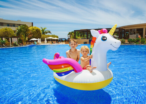 Happy siblings on a swimming unicorn in the hotel pool - summer vacation