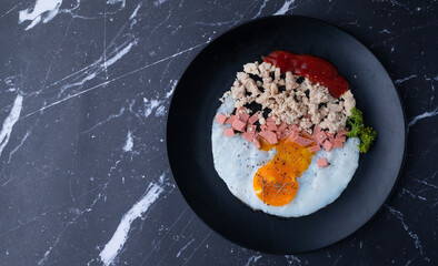homemade american breakfast, fried egg, sausages, and minced pork with ketchup tomato sauce on marble table, food styling concept on dark black background.