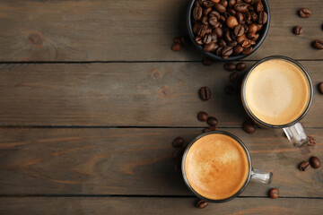 Cups of hot aromatic coffee and roasted beans on wooden table, flat lay. Space for text