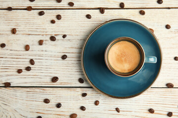 Cup of hot aromatic espresso and roasted beans on white wooden table, flat lay