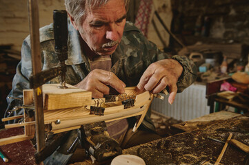 Craftsman in workshop making wooden toy, a wooden model of sailboat. Carpenter sticks a wooden part on a wooden ship