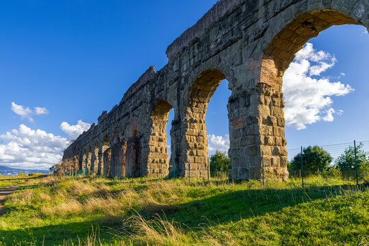 Park of the Aqueducts Rome, the imposing arches of the Claudio with blue sky and clouds and shadows reflected on the lawn. Archaeological area water system of ancient Rome. Via Appia Regional Park.