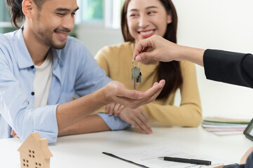 Young Asian couple feeling happy after finish buying or rental real estate with agent and receiving house key after sign contract. Real estate business or Asian urban lifestyle concept.