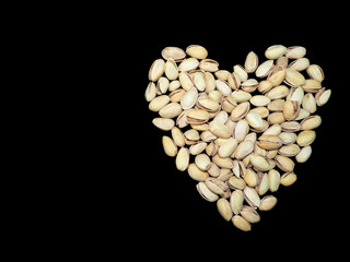 on the right, many pistachio seeds are laid out in the shape of a heart on a black background . top view