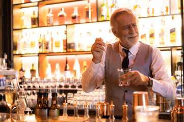 professional bartender mixinig cocktail for customer at counter, barman nightlife concept, Shelves with bottles of alcohol in background.