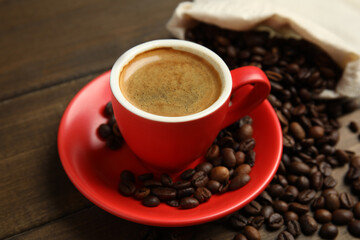 Cup of tasty coffee and beans on wooden table