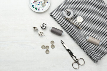 Flat lay composition with different sewing supplies and fabric on white wooden table. Space for text