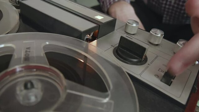 Male disc jockey presses buttons on reel to reel tape recorder at school retro disco. Olds chool concept. Popular Disco Trends 60s, 70s, 80s, 90s. On a plank floor. Vintage Tape Recorder.