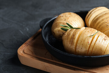 Raw Hasselback potatoes with rosemary in baking pan on dark grey table, closeup. Space for text