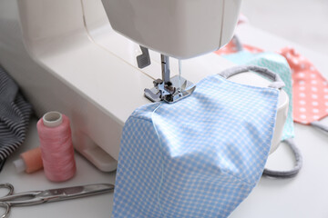 Sewing machine with cloth mask on white table, closeup