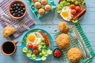 composition of rustic breakfast, eggs and sausage with vegetables, roll and coffee, wooden background, top view