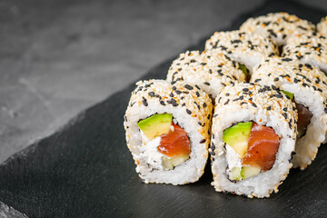appetizing california sushi roll with cheese avocado cucumber and salmon in sesame seeds on a black stone plate