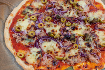 High angle view detail closeup studio shot of freshly baked pizza al tonno on baking paper. Olives, tuna, onion, veggies, crust.