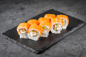 appetizing sushi roll philadelphia with avocado cheese eel cucumber and salmon on a black stone plate