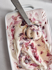 White ceramic ice cream container with homemade macerated black cherry and white chocolate ice cream. A vintage ice cream scoop is dragged through the top with a scoop of ice cream in it. 