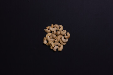 A handful of cashews on a black background. The nuts are folded in order. Background for the label. Light walnut.