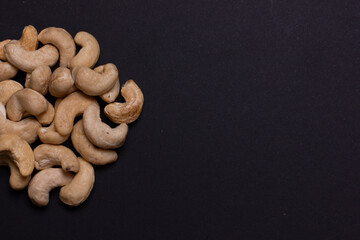 A handful of cashews on a black background close-up. A pile of light nuts. Free space for the...