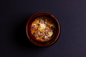 Ceramic pot with buckwheat porridge on a black background. An empty space for the inscription. Top view of a pot of buckwheat porridge.